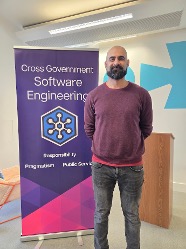 Asim Hussain standing near banner at the Cross Government Software Engineering Conference