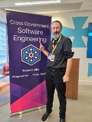 Terence Eden standing near banner at the Cross Government Software Engineering Conference